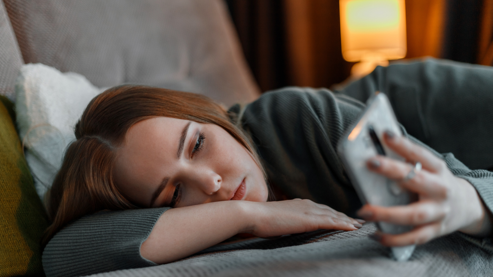 Girl suffering from insomnia with nighttime light from surfing Internet or chatting using smartphone at night lying on bed