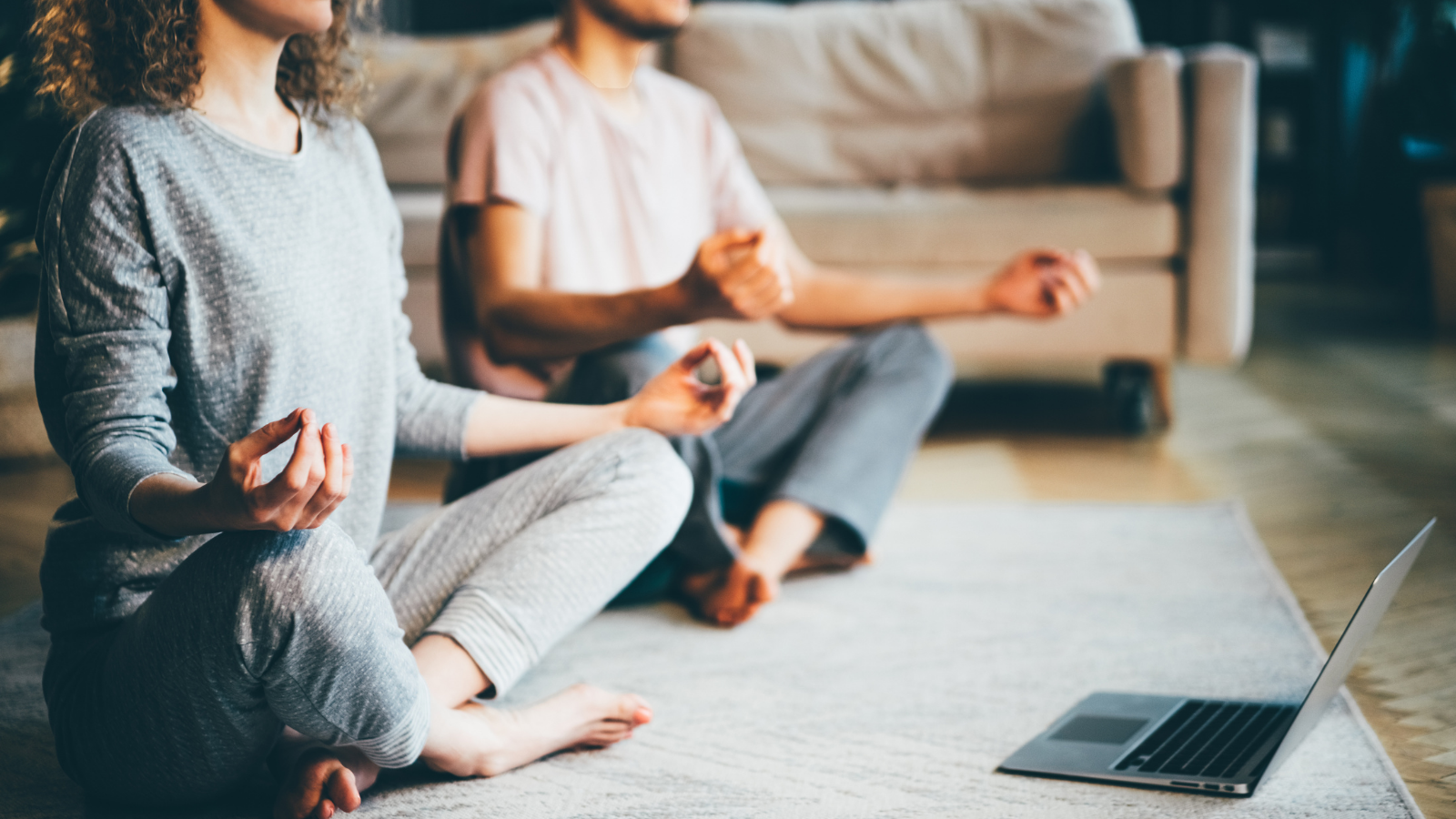 Calm couple in pajamas meditating, listening spiritual practices lessons on laptop, sitting in Lotus Pose at home